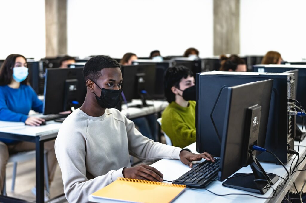 Young multiracial students taking an exam in high school while wearing face mask